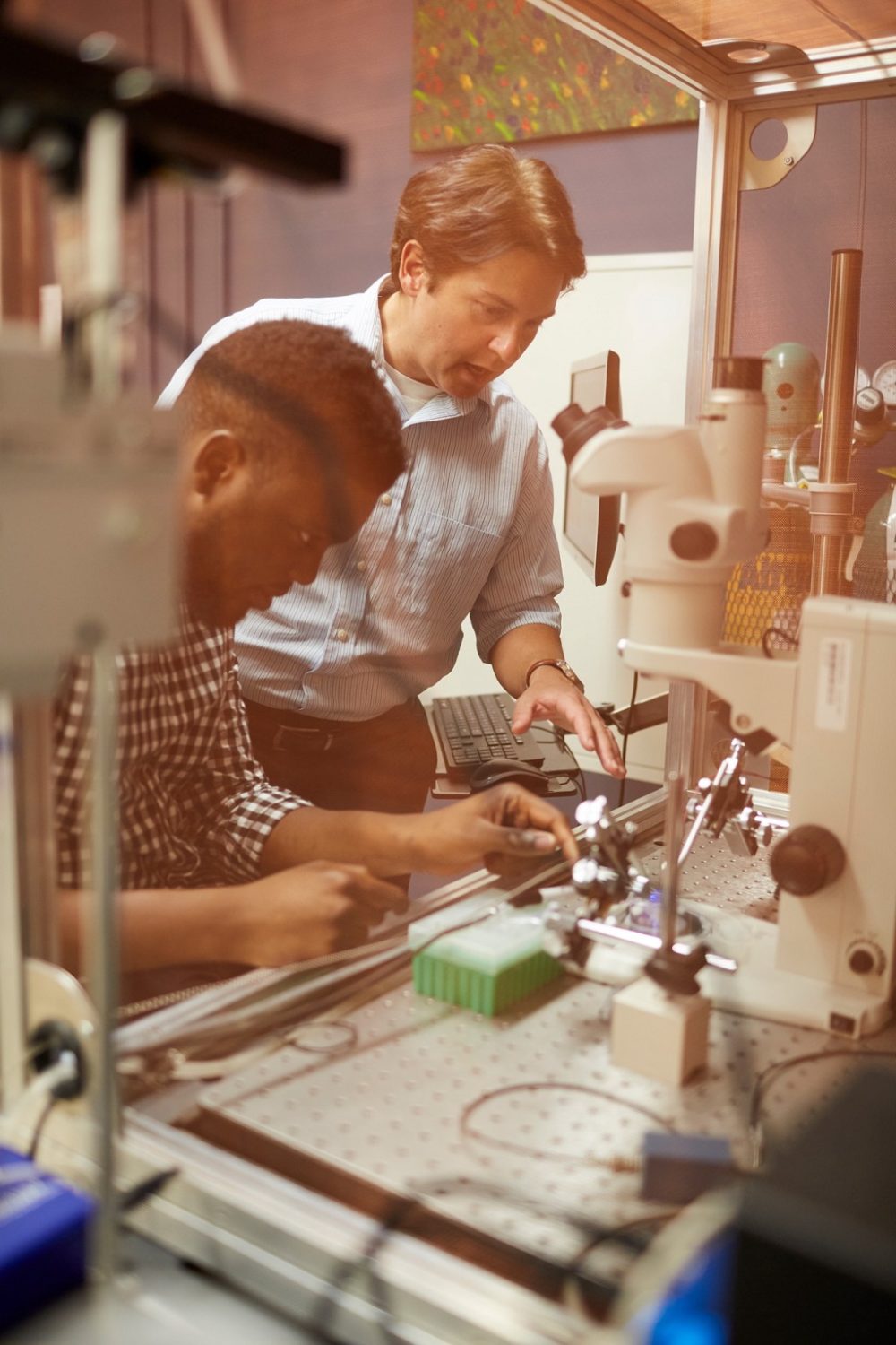 Kacy Cullin talking to Dayo Adewole in a lab filled with various metal and plastic equipment.