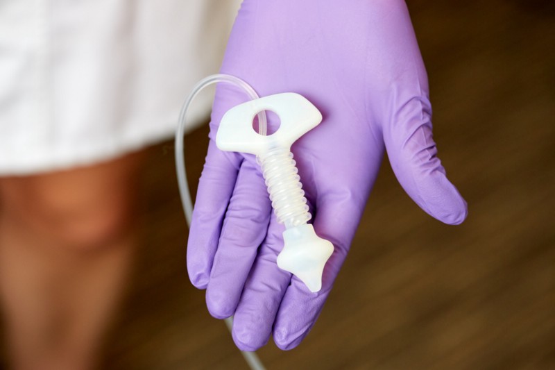 A purple-gloved hand holding white anal probe device.